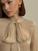 Beige skjorta med långa utsvängda ärmar och rosett i halsen